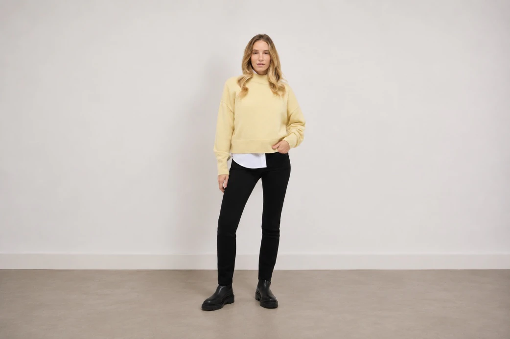 Model in schwarzer Straight Leg Jeans mit gelbem Pullover und schwarzen Boots