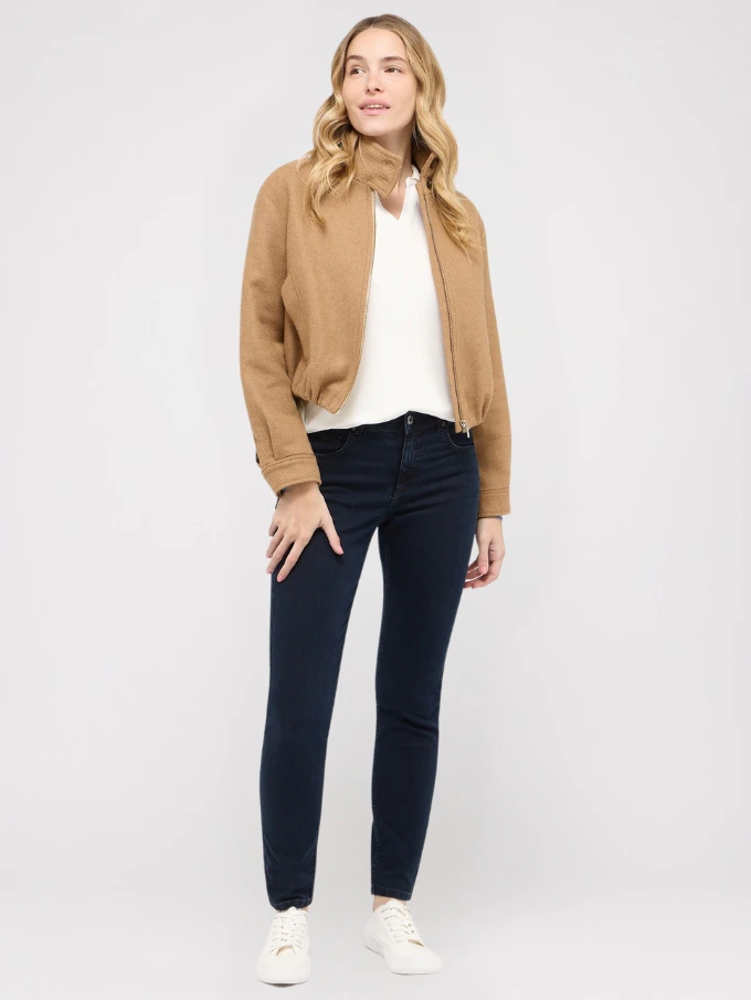 Model trägt dunkelblaue Skinny Jeans von ANGELS mit beiger Jacke und weißen Sneakern.