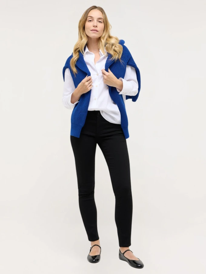 Model trägt schwarze ANGELS Skinny Jeans kombiniert mit weißer Bluse, blauem Strick und Ballerinas.