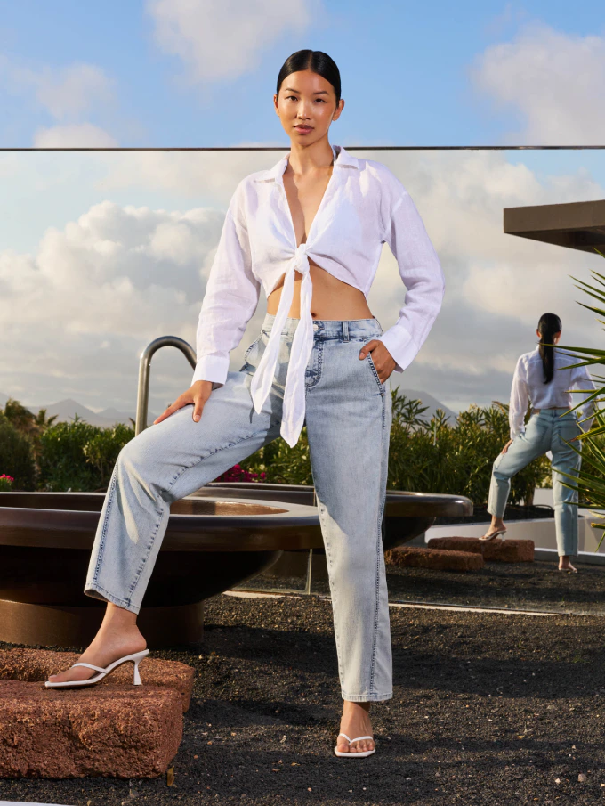 Frau in heller Angels Jeans und weißer Bluse auf sonniger Terrasse
