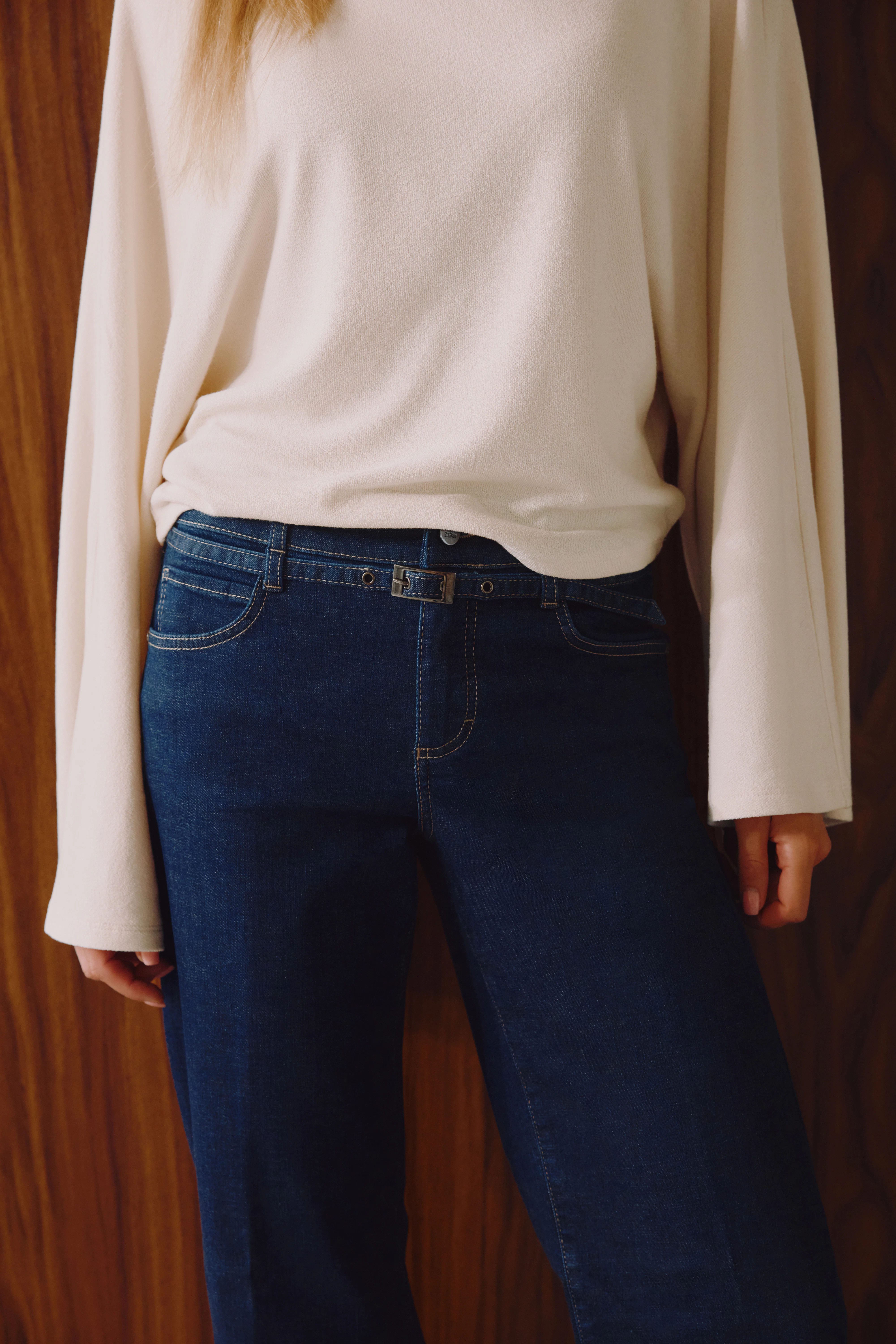 Detailaufnahme einer dunkelblauen Jeans mit schmalem Gürtel und hellem Pullover