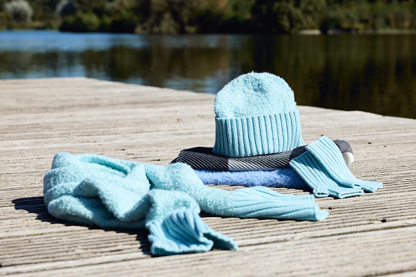Winteraccessoires in turkoois, liggend op een steiger aan het water.