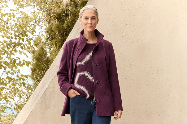 Eine Frau in blauer Jeans, gemustertem Pullover und bordeaux Jacke. 