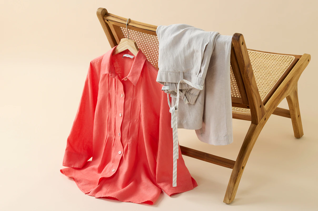 Eine koralle Bluse und eine neutrale Leinenhose hängend über eine Stuhllehne.   