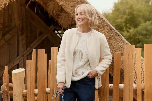 Een vrouw in een blauwe spijkerbroek, een beige trui en een bontjas.