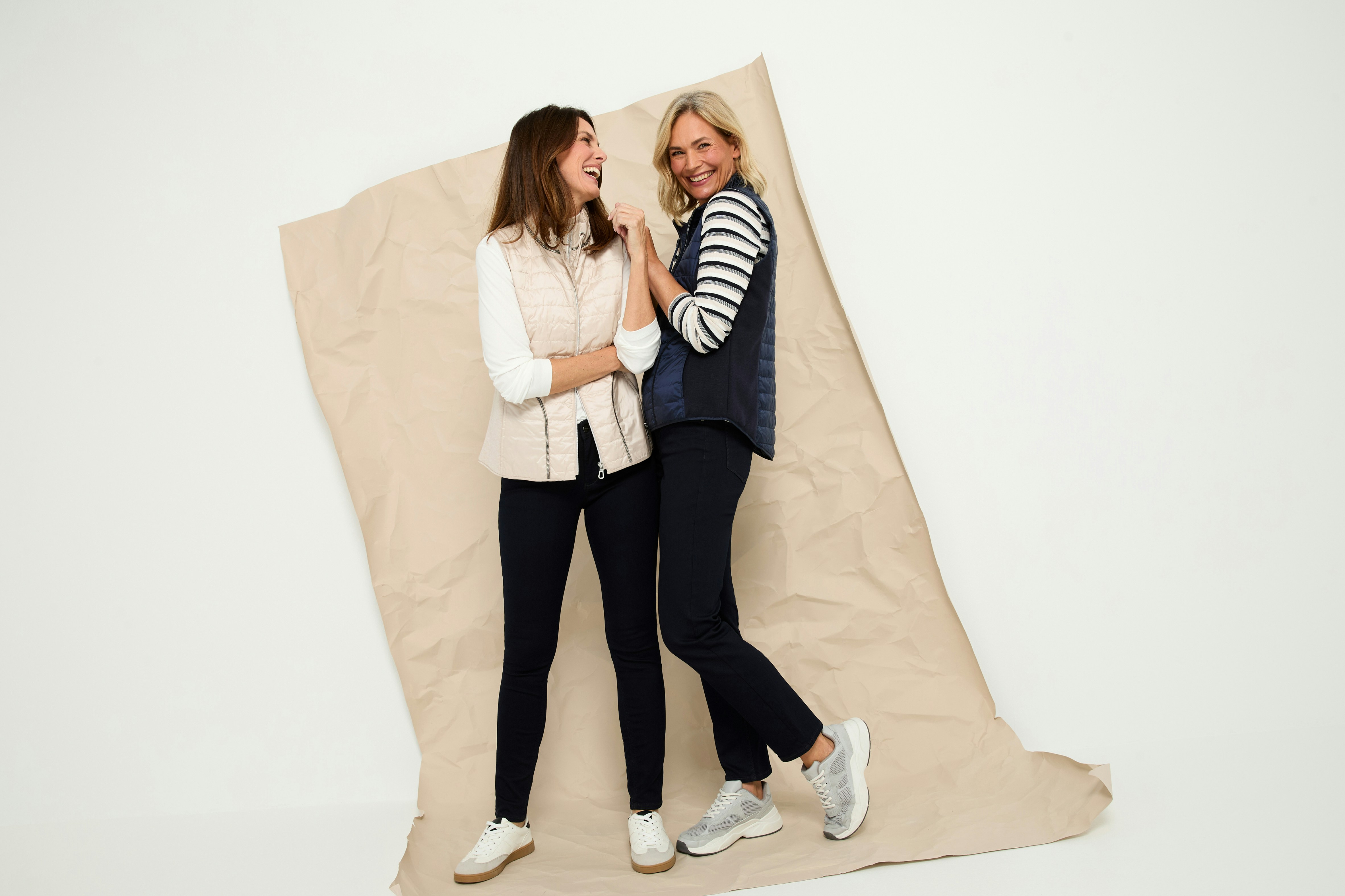 Zwei Frauen mit Outfits bestehend aus Weste, Pullover und Jeans. 