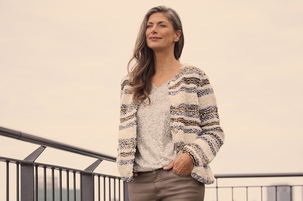Eine Frau mit einem Glitzershirt und gestreifter Strickjacke und einer Hose in Lederoptik. 