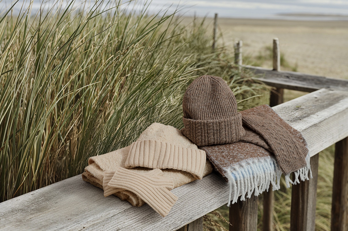 Gebreide sjaal, muts en wanten liggen op een houten hek.