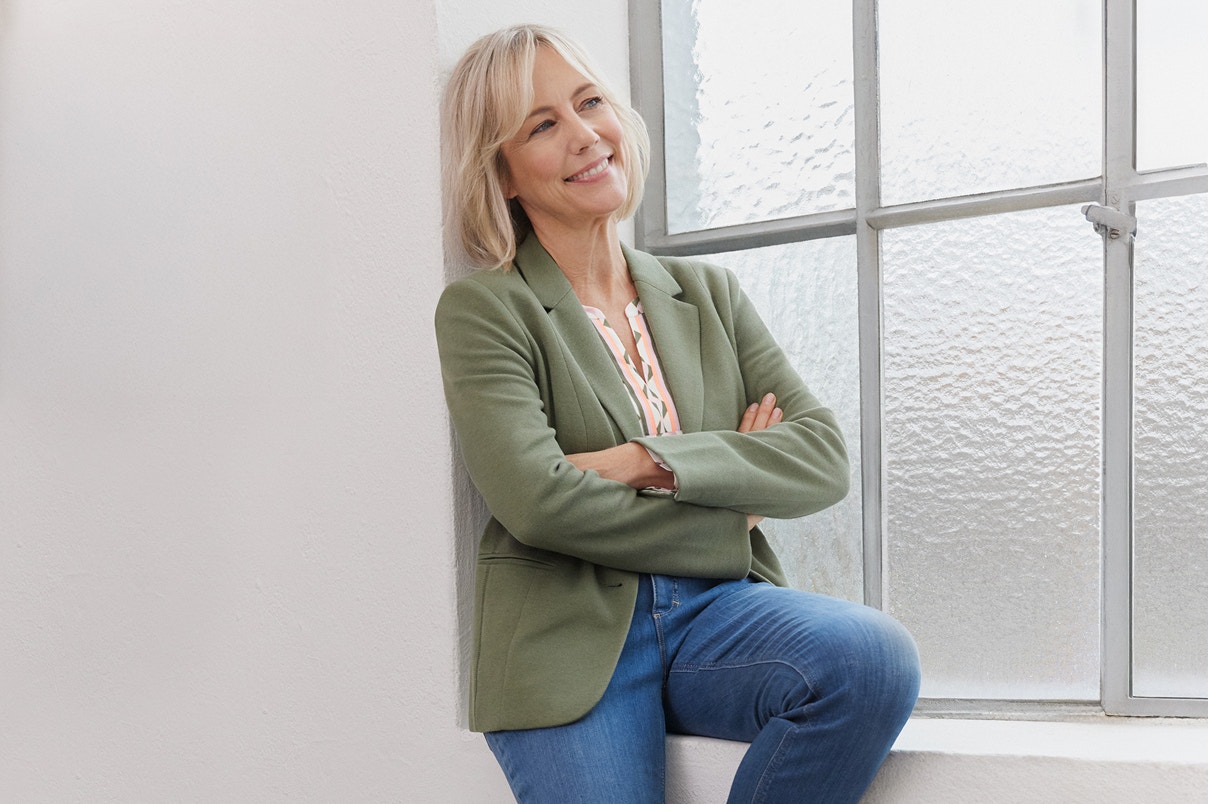 Eine Frau sitzend auf einer Fensterbank in einem neuen Bonita Blazer und blauer Jeans. 