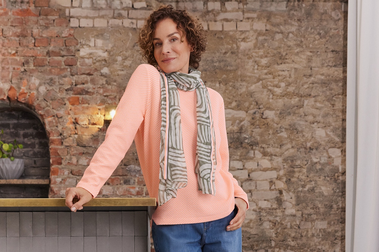 Eine Frau stehend in einer blauen Bonita Jeans mit Pullover und Schal. 