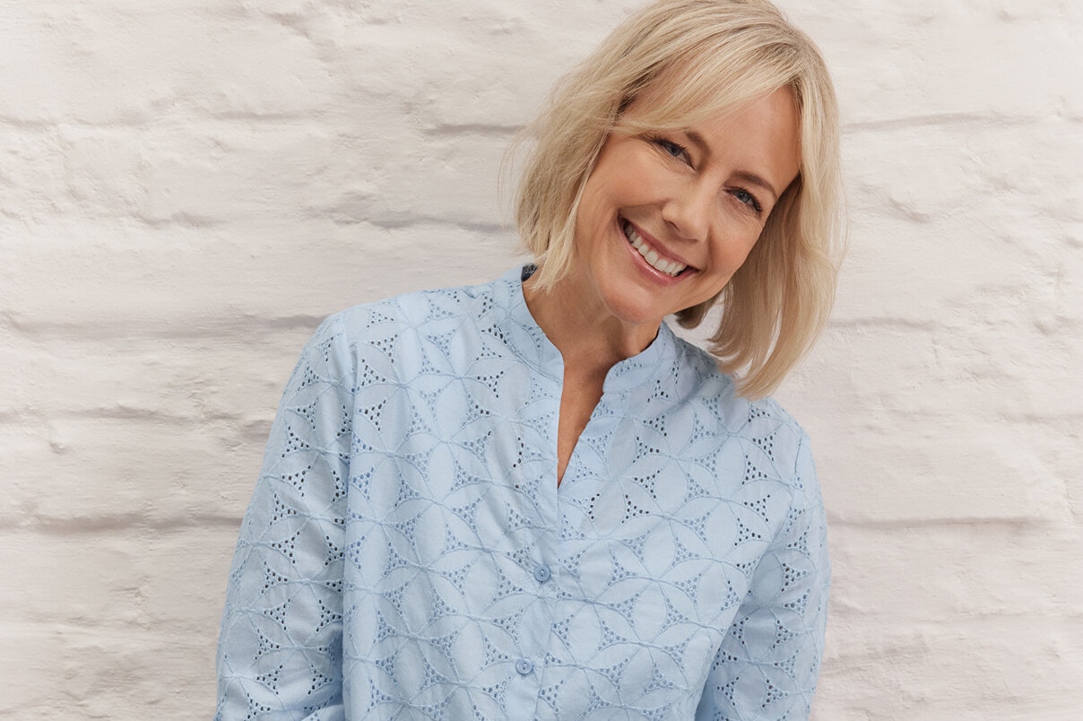 Een vrouw in een nieuwe Bonita-blouse met borduursels en een blauwe spijkerbroek.  