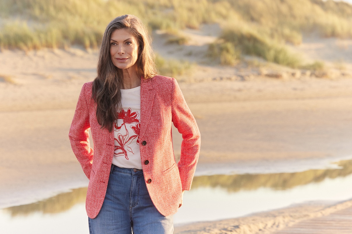 Eine Frau stehend in einer blauen Bonita Jeans, einem weißem Shirt mit rotem Print und einem roten Blazer.   
