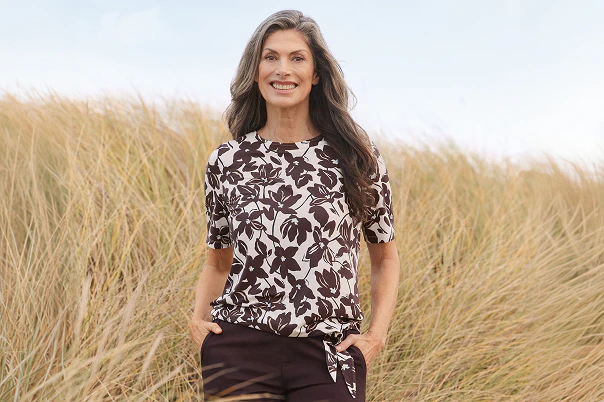 Eine Frau stehend in einer braunen Hose mit geblümten Shirt.  