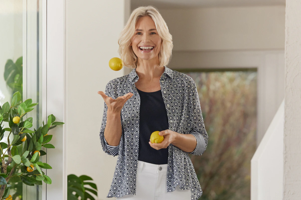 Een vrouw staat daar in een witte capribroek, een topje en een blouse met een patroon. 