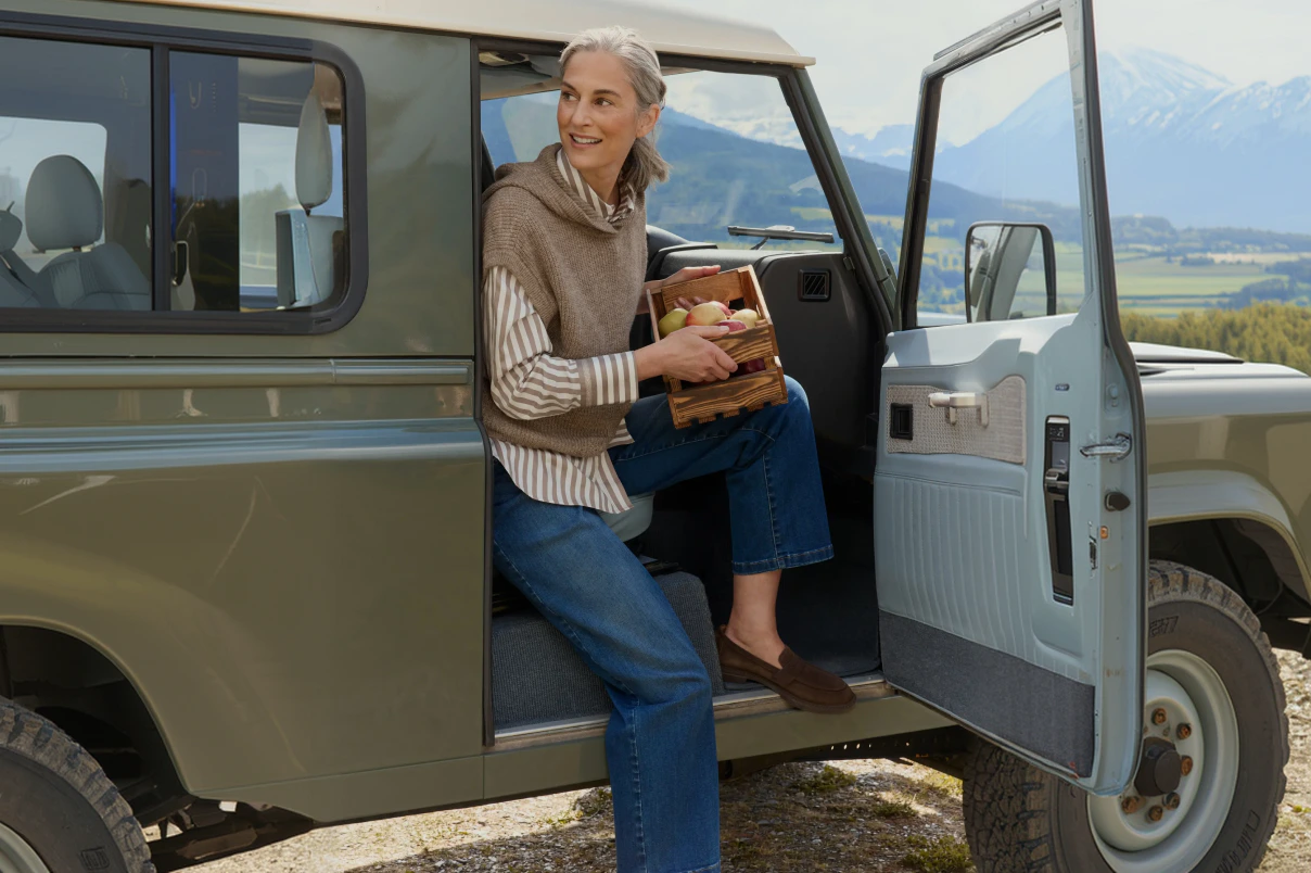 Eine Frau in blauer Jeans, gestreifter Bluse und einem beigen Strickpullunder. 