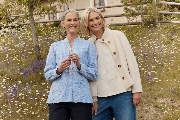 Zwei Frauen stehend in blauer Jeans, blauer Bluse und beiger Jacke.