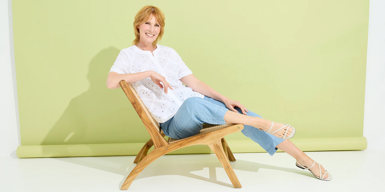 Een vrouw in een spijkerbroek en een witte blouse met borduursels.  