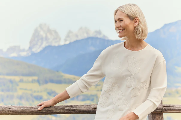Eine Frau einem beigen Sweatshirt mit Blütenapplikationen. 