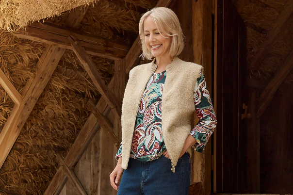 Een vrouw in een blauwe spijkerbroek, een shirt met patroon en een beige bontvest.