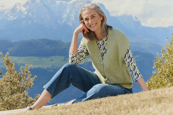 Eine Frau in Jeanshose und gemustertem Shirt und einem grünen Pullunder.