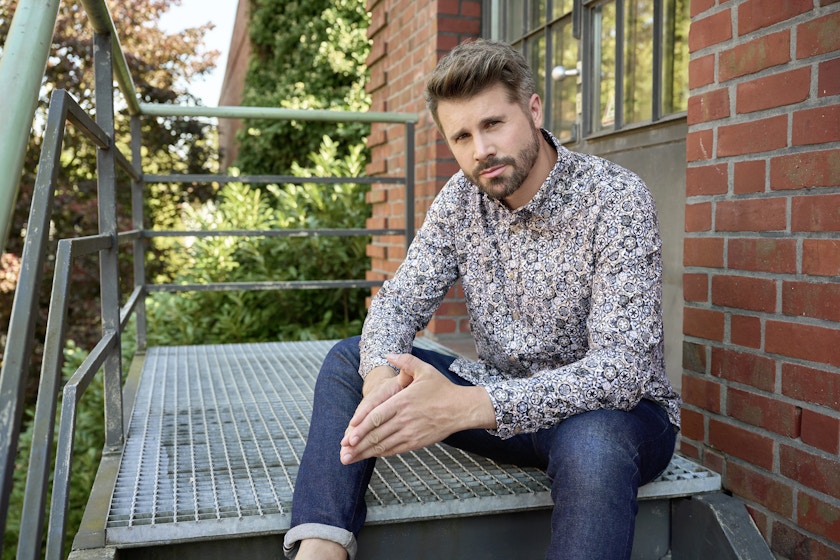 Thore Schölermann sitzt auf einer Treppe mit einem Freizeithemd von CASAMODA