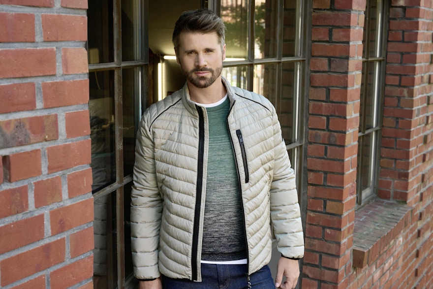 Mit einer beigen Steppjacke und einem grünen Pullover von CASAMODA posiert Thore Schölermann