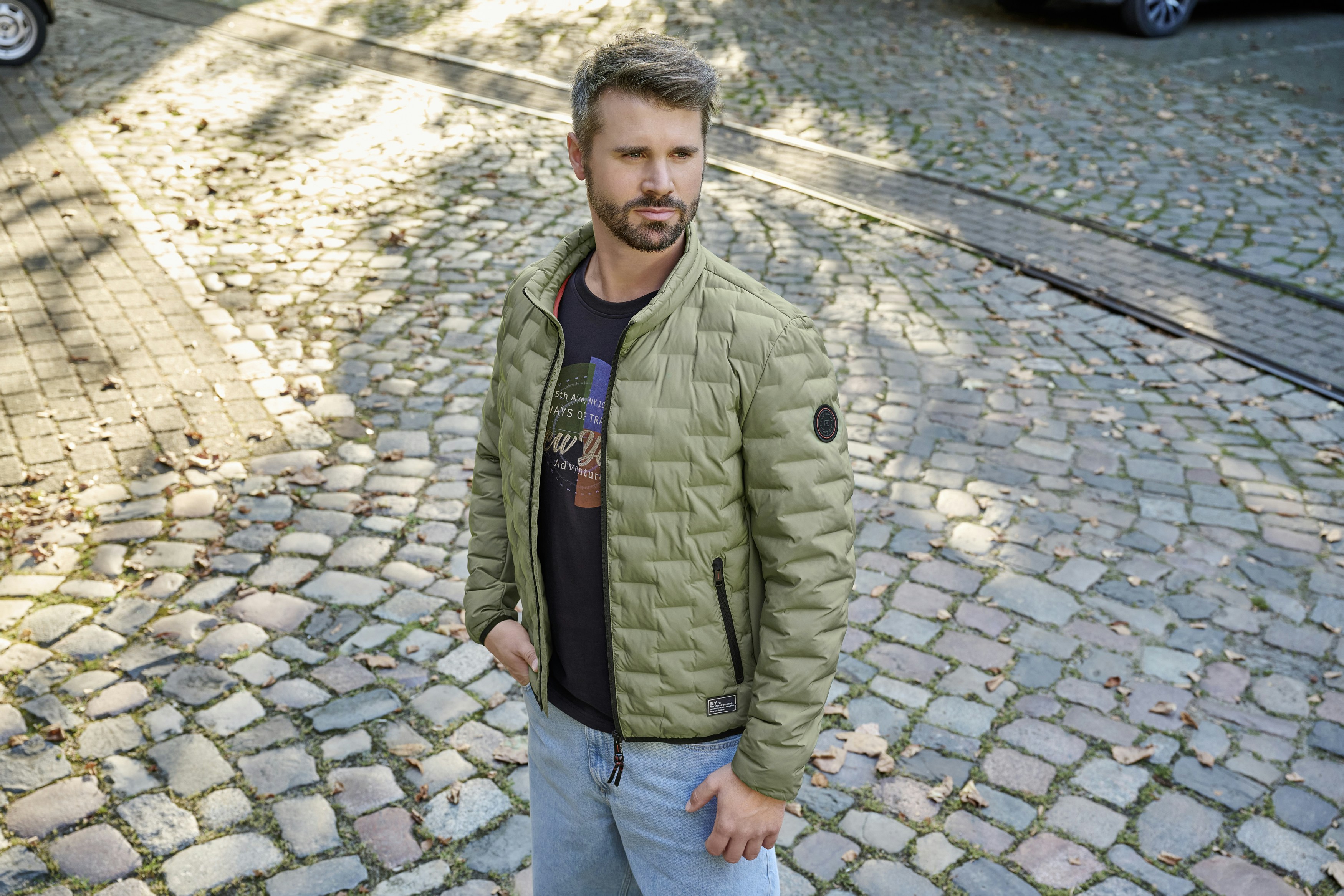 Thore Schölermann steht auf der Strasse mit einer grünen Steppjacke von CASAMODA