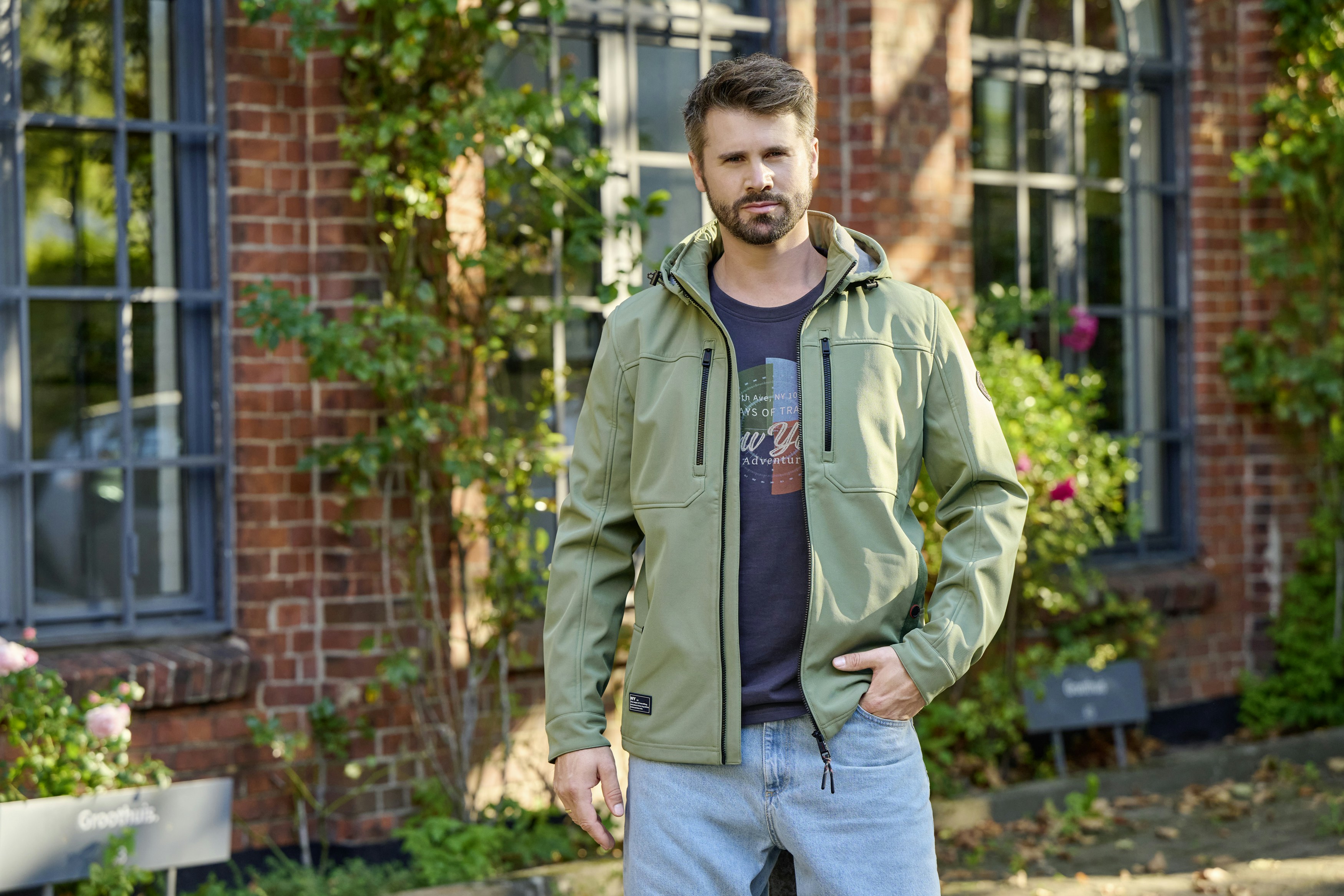 Thore Schölermann posiert vor einem Haus in einer grünen Sweatjacke von CASAMODA