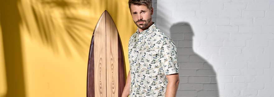 Thore Schölermann posiert vor einem Surfbrett in einem Freizeithemd von CASAMODA