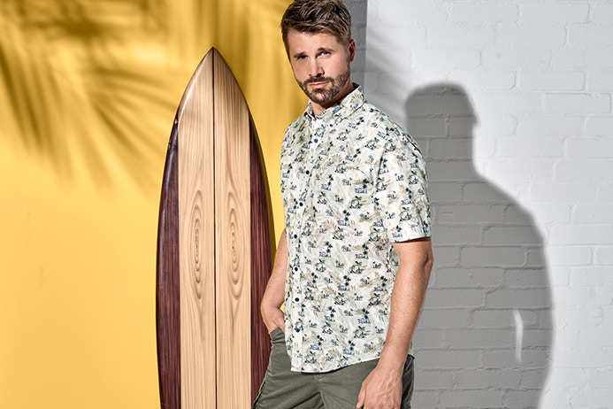Thore Schölermann posiert vor einem Surfbrett in einem Freizeithemd von CASAMODA
