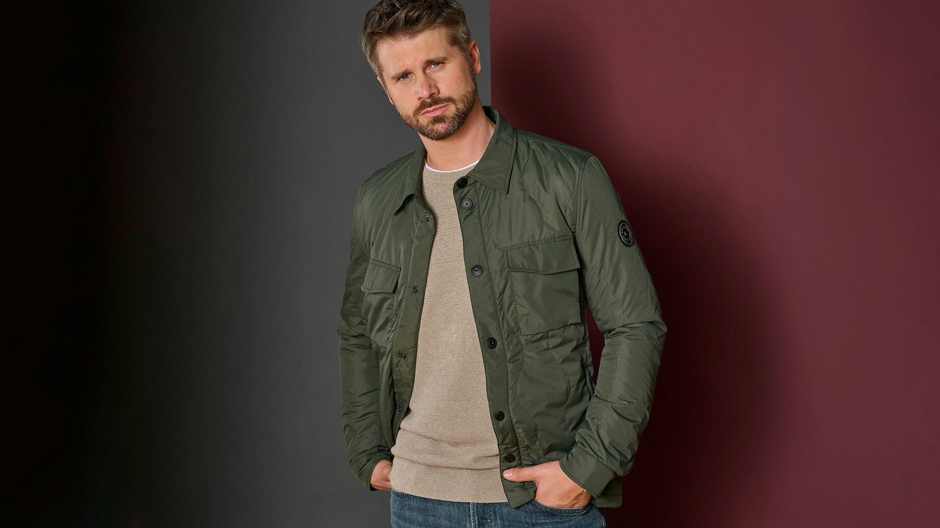 Thore Schölermann posiert vor einem Haus mit einer grünen Overshirtjacke von CASAMODA.