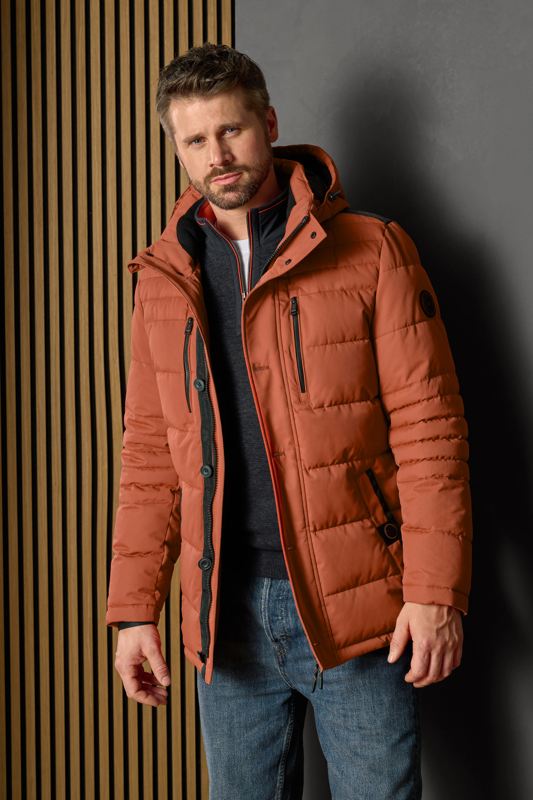 Thore Schölermann posiert mit einer orangenen Winterjacke von CASAMODA