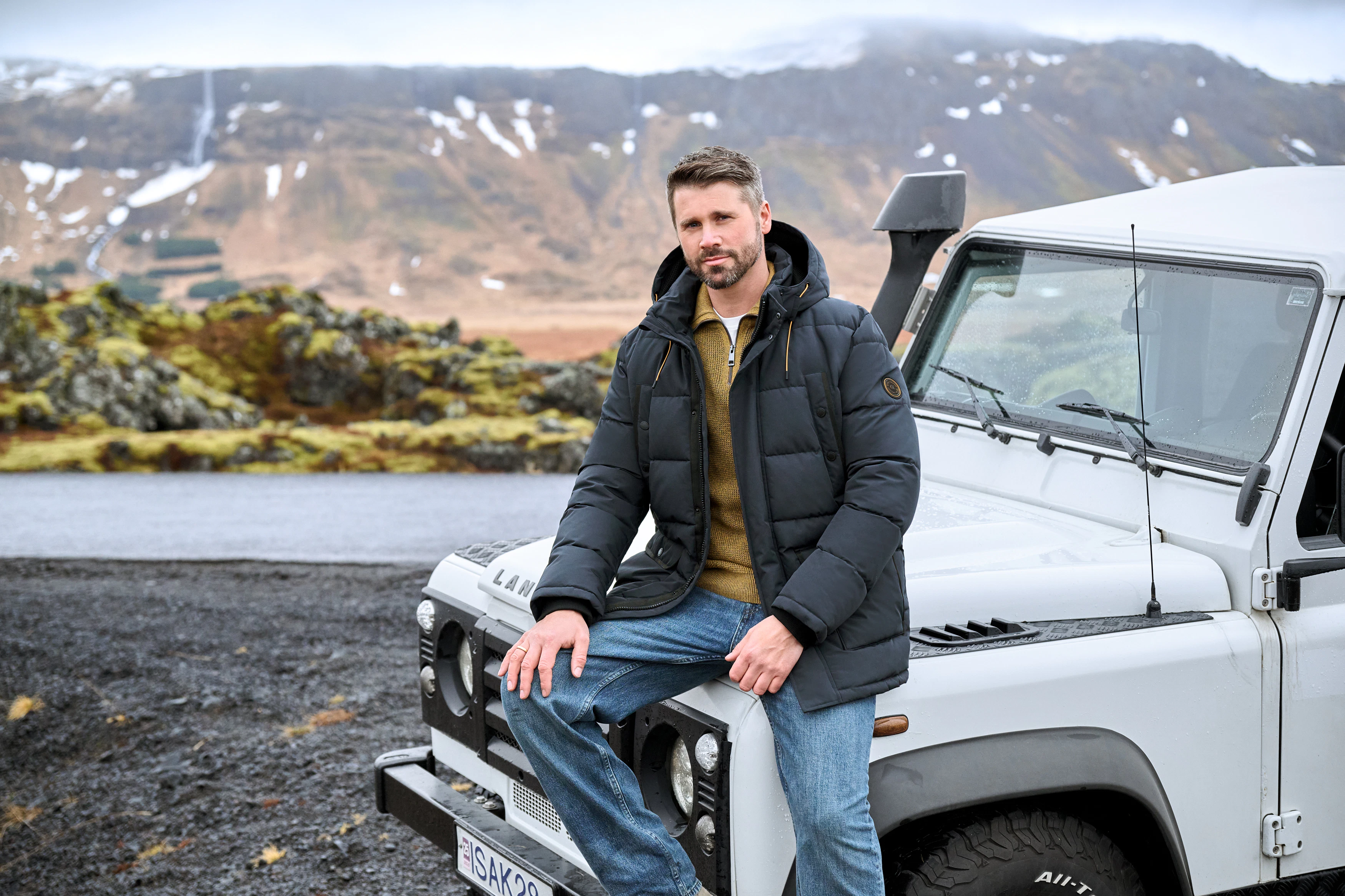 Thore Schölermann sitzt auf einem weißen Auto mit einer blauen Winterjacke von CASAMODA
