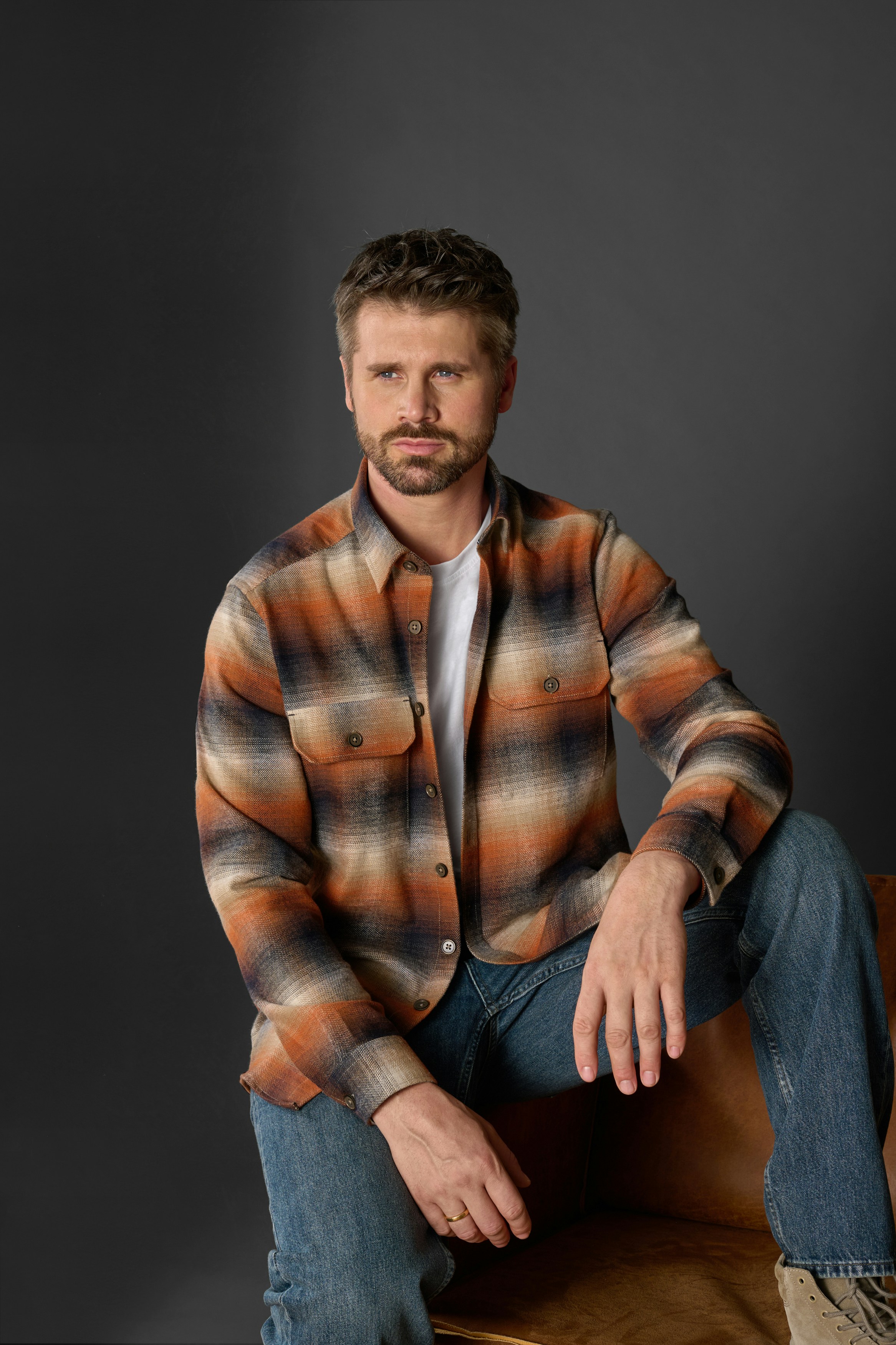 Thore Schölermann sitzt auf dem Sessel mit einem orangenen Overshirt von CASAMODA