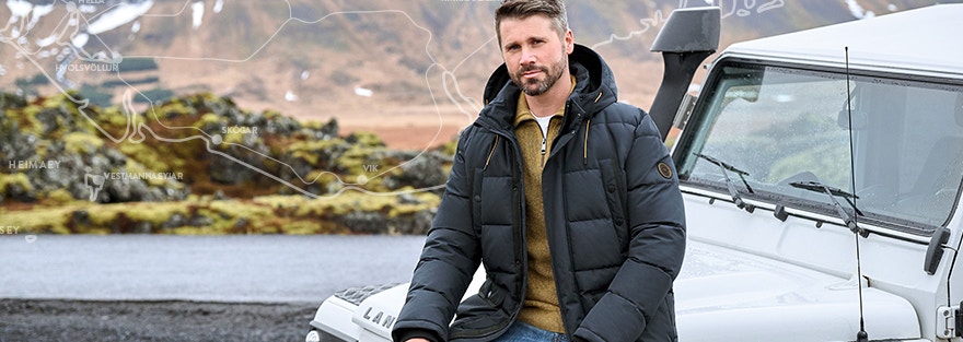 Thore Schölermann sitzt auf einem weißen Auto mit einer blauen Winterjacke von CASAMODA