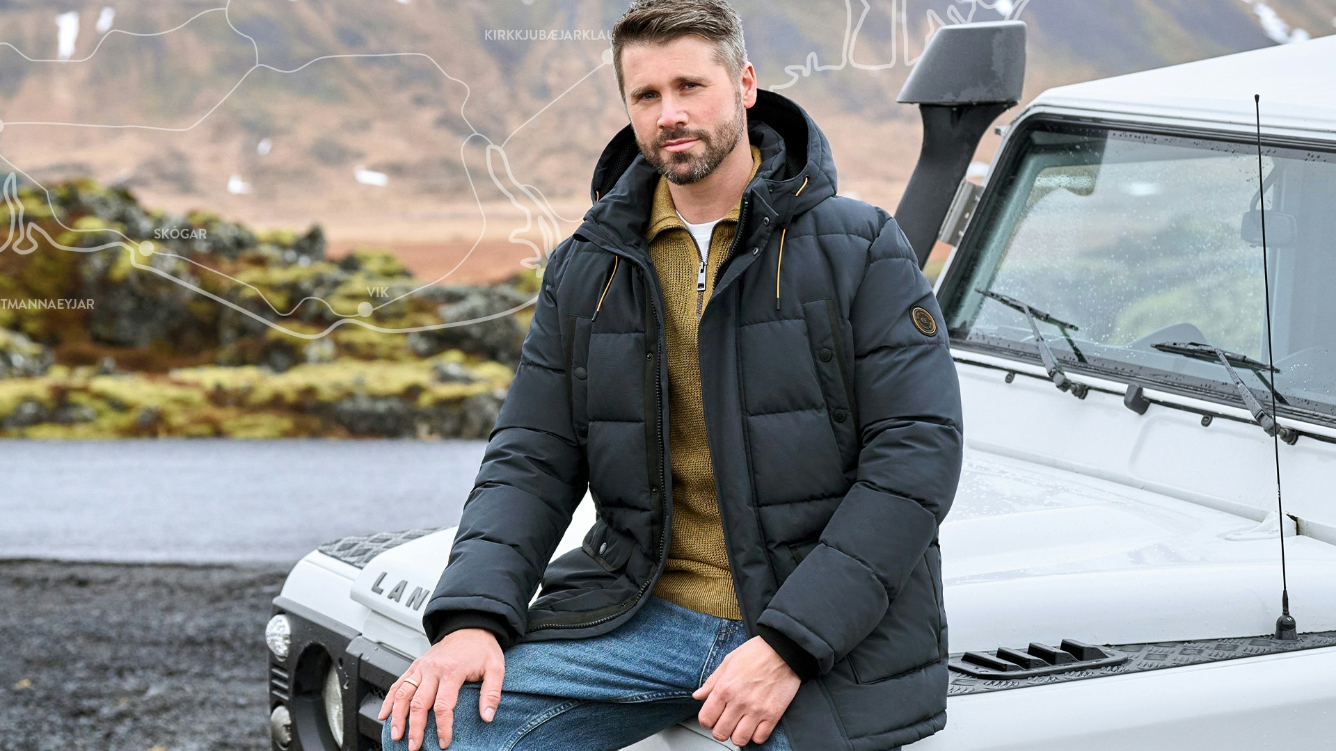 Thore Schölermann sitzt auf einem weißen Auto mit einer blauen Winterjacke von CASAMODA