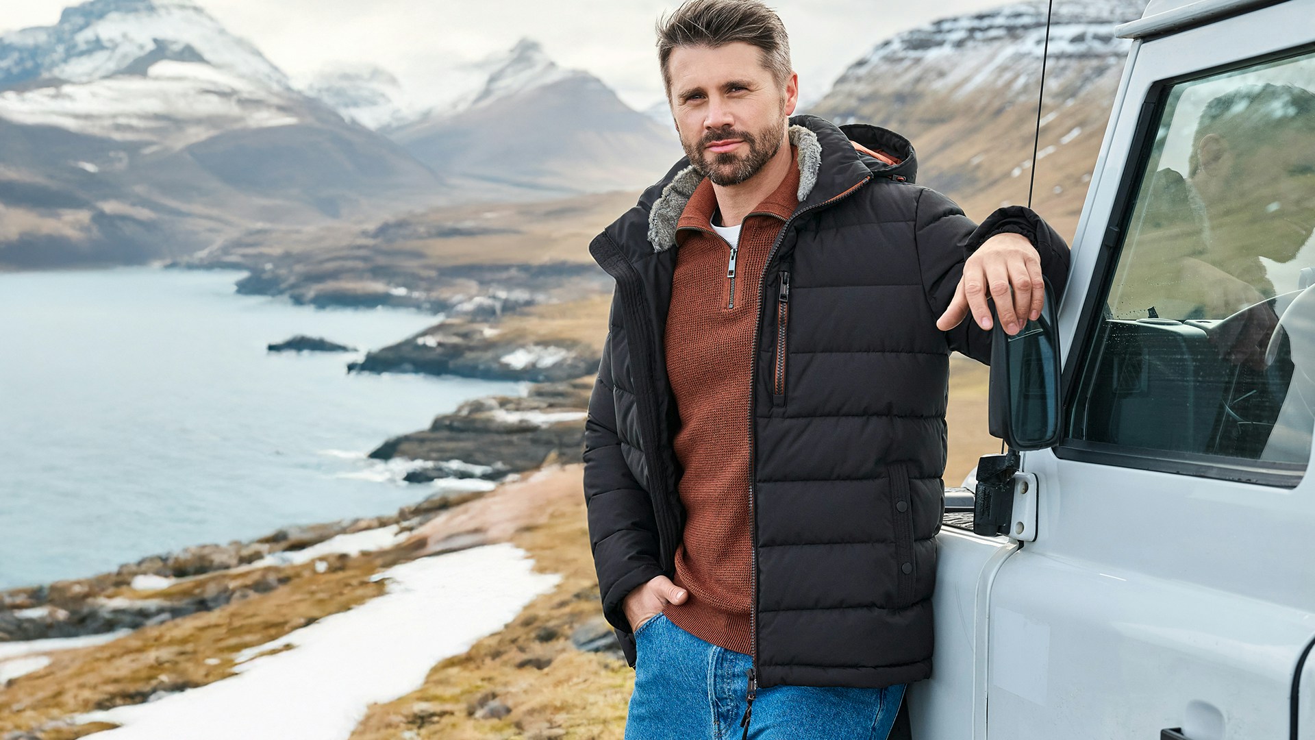 Thore Schölermann in Casamoda Jacke am Jeep mit Bergkulisse im Hintergrund