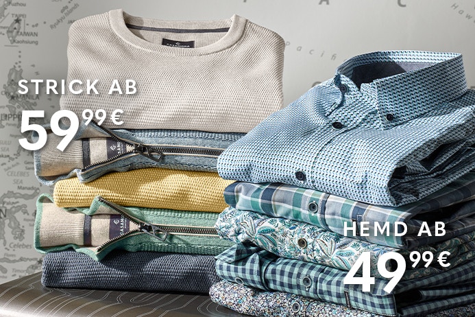 Gestapelte Oberteile und Hemden in verschiedenen Farben und Mustern liegen auf einem Koffer. Im Hintergrund ist eine Weltkarte zu sehen.