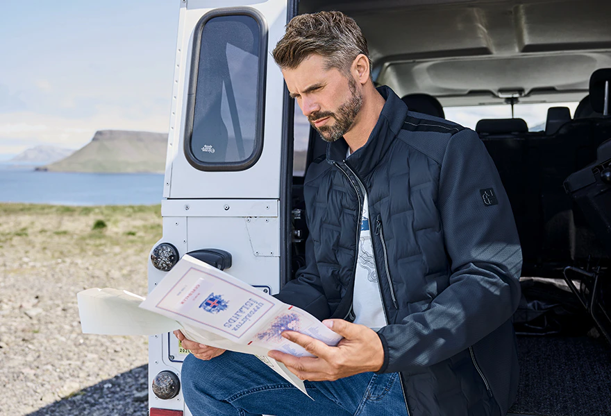 Thore Schölermann sitzt an der offenen Tür eines weißen Geländewagens und hält eine aufgefaltete Karte in den Händen