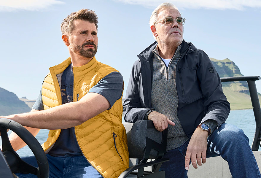 CASAMODA Herrenmode: Mann in gelber Steppweste neben Mann in blauer Jacke auf einem Sitz