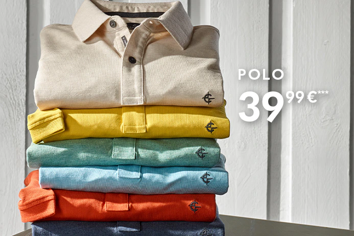 Mehrere gefaltete Poloshirts in verschiedenen Farben sind übereinander gestapelt. Rechts daneben steht ein Kompass auf einem Koffer, der Hintergrund besteht aus einer hellen Wand.