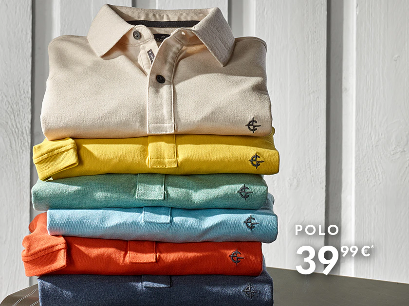 Mehrere gefaltete Poloshirts in verschiedenen Farben sind übereinander gestapelt. Rechts daneben steht ein Kompass auf einem Koffer, der Hintergrund besteht aus einer hellen Wand.