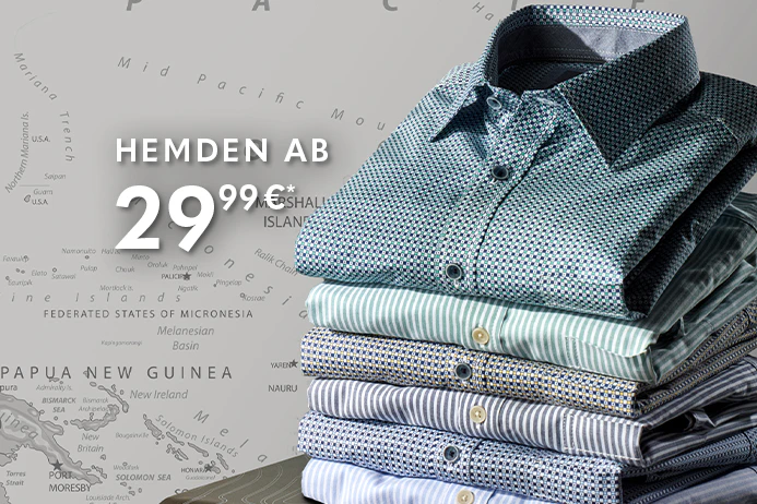 Gestapelte Hemden in verschiedenen Farben und Mustern liegen auf einem Koffer. Im Hintergrund ist eine Weltkarte zu sehen.