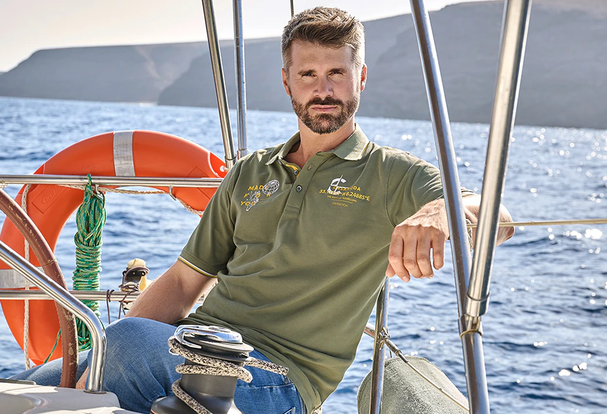 Herren Poloshirt in Oliv mit Logo-Print auf einem Segelboot vor dem Meer