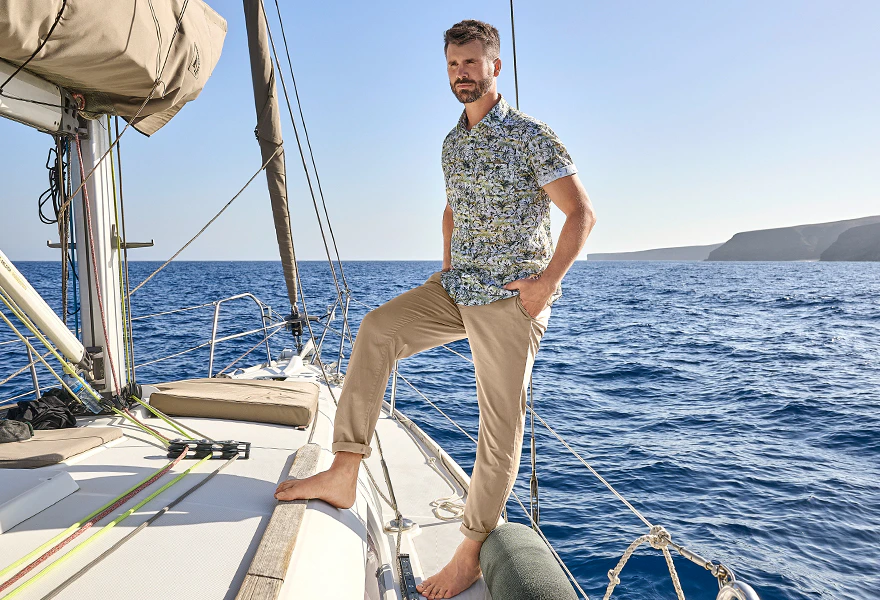 Herren Kurzarmhemd mit Allover-Print und beige Chino auf einem Segelboot vor Küstenkulisse