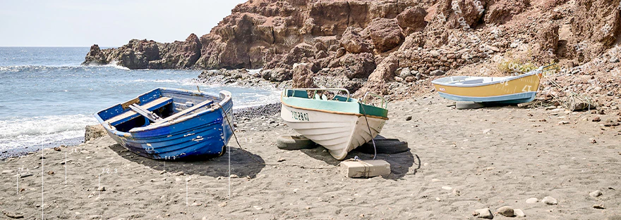 Drei Boote liegend am Strand mit einer Küstenlandschaft im Hintergrund