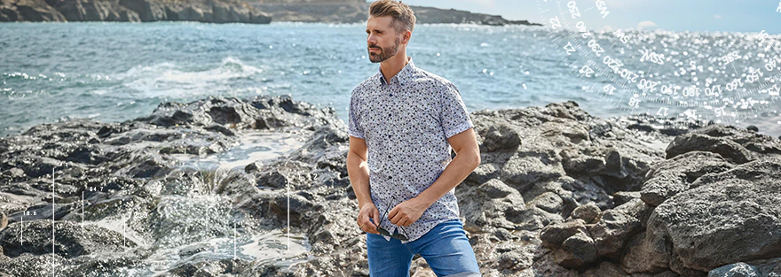 CASAMODA Kurzarmhemd mit blauem Muster und Jeansshorts an felsiger Meeresküste