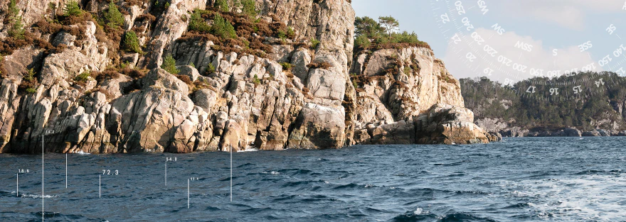 Felsige Küstenlandschaft am Meer mit schroffen Klippen und bewachsenen Felsen.