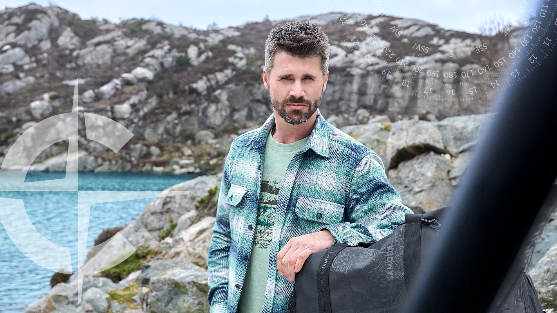 Thore Schölermann trägt ein grün-blau kariertes Overshirt über grünem Print-T-Shirt vor einer felsigen Küste.