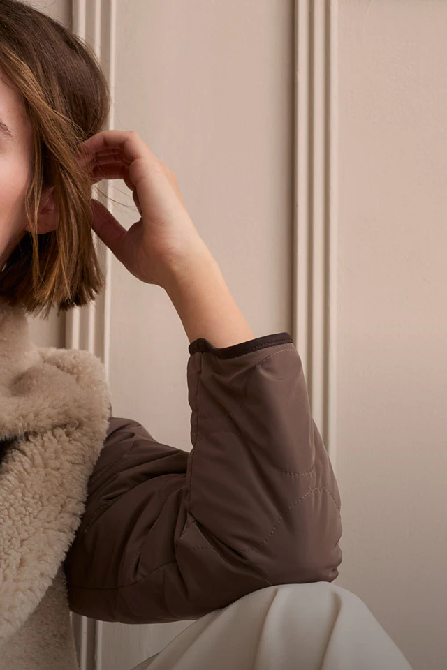 Model wearing a beige jumper and a brown jacket with teddy fur.